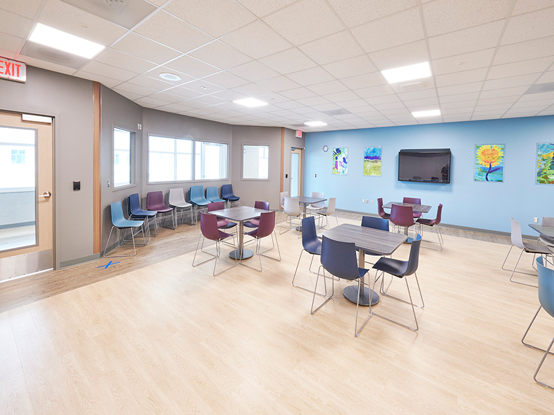 A room with tables, chairs, and bright paintings on the walls at Tower Behavioral Health